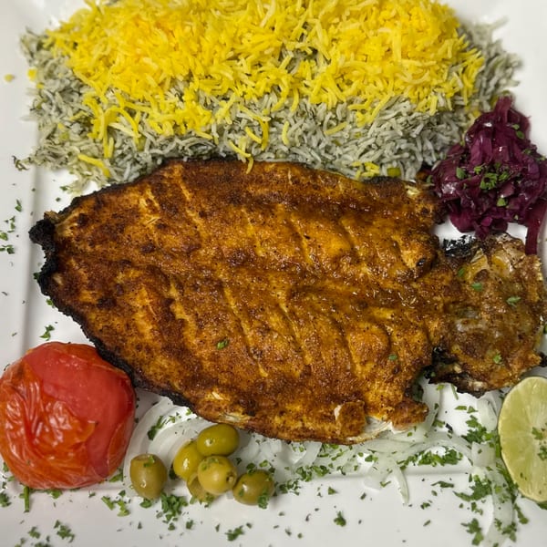 A whole grilled fish with saffron and dill rice, pickled cabbage, tomato, olives, and lime.