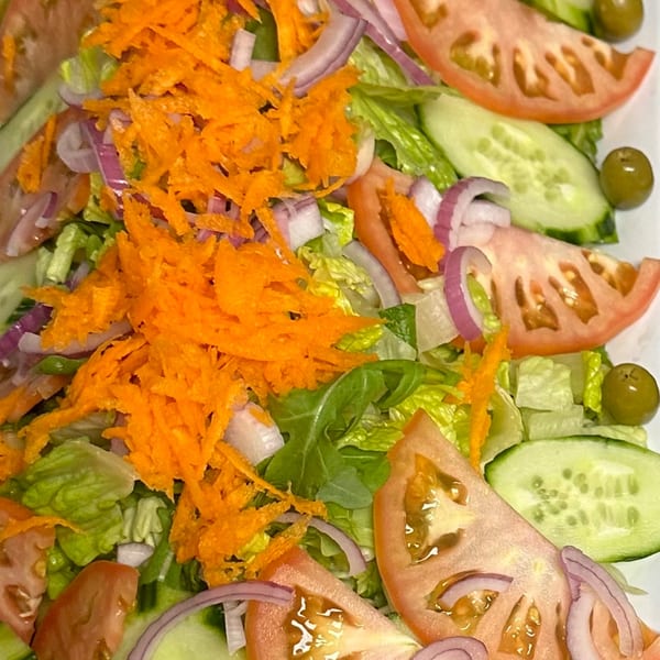 A fresh Persian salad with lettuce, tomatoes, cucumbers, red onions, shredded carrots, and olives.