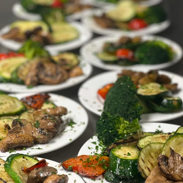 Multiple plates of grilled vegetables, including zucchini, mushrooms, broccoli, and red peppers, garnished with parsley.