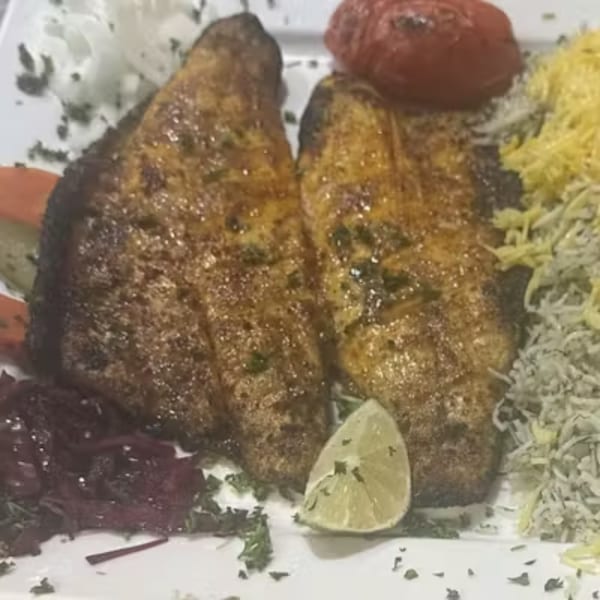 Two pieces of grilled fish with rice, a roasted tomato, and a lime wedge.