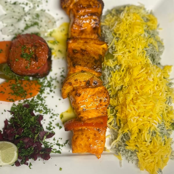 Persian chicken kebab skewer with saffron rice, grilled tomato, and fresh herbs on a white plate.