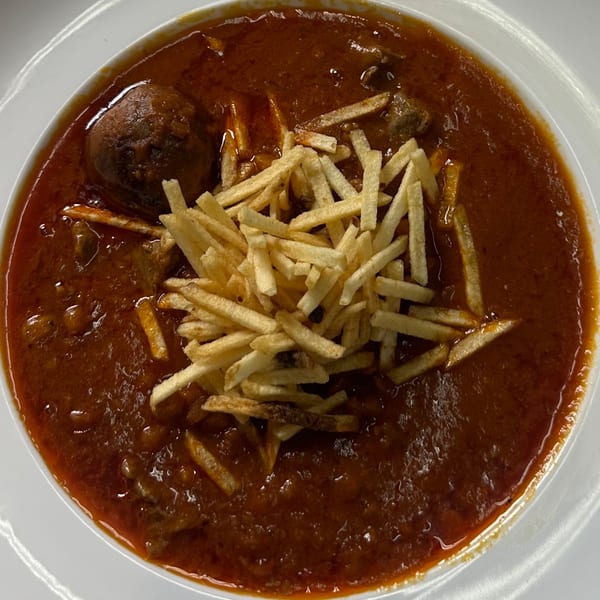A bowl of Persian ghormeh sabzi stew with a meatball and topped with crispy shoestring fries.