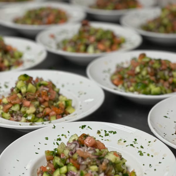 Multiple white plates filled with fresh Shirazi salad, featuring diced cucumbers, tomatoes, and onions.