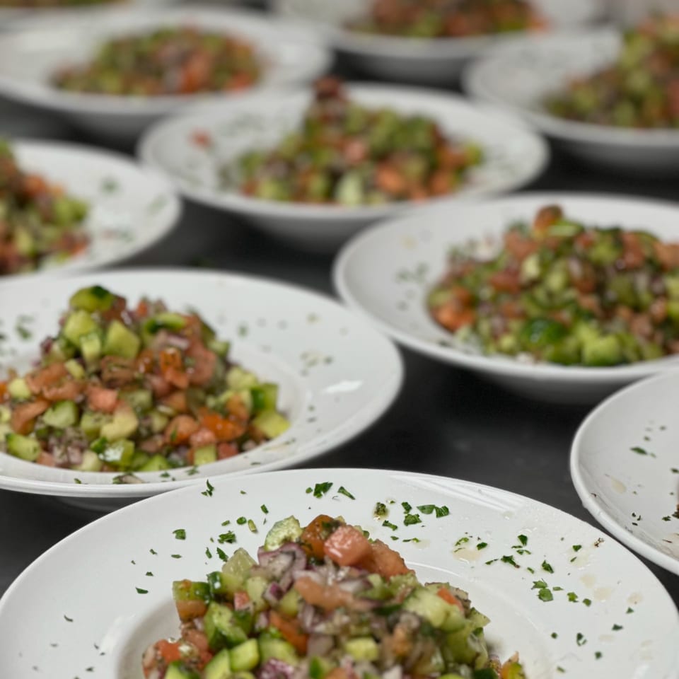 Multiple white plates filled with fresh Shirazi salad, featuring diced cucumbers, tomatoes, and onions.