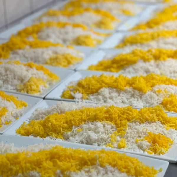 Rows of white and yellow Persian rice portions on rectangular plates, ready to be served.