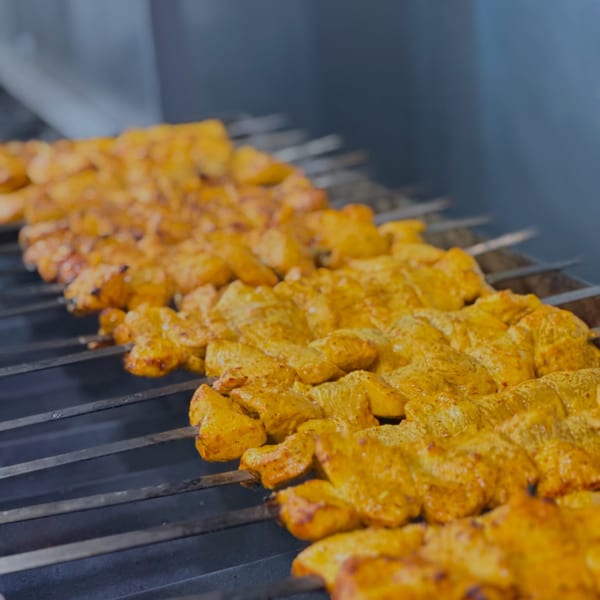 Rows of golden Persian chicken kebabs grilling on metal skewers at Parisa Persian Grill.