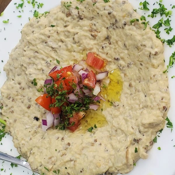 Kashk Bademjan, a Persian eggplant dip, garnished with diced tomatoes, red onions, and parsley.