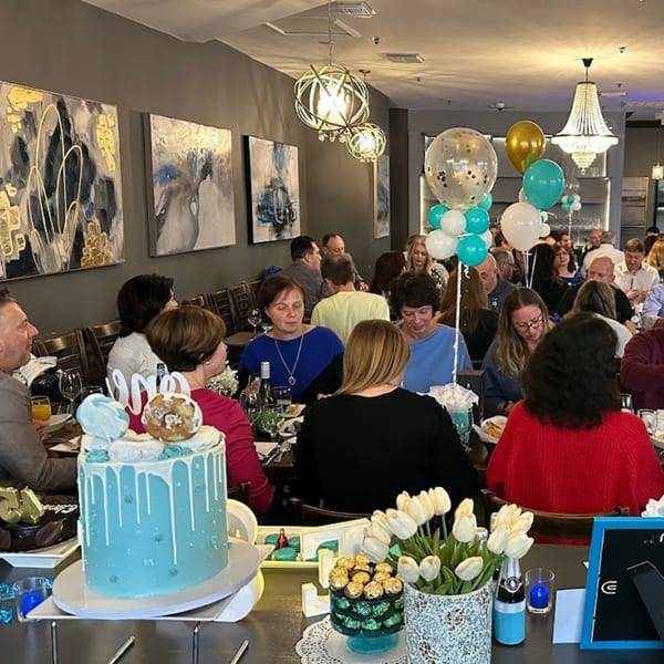 A large group of people celebrating with cakes and balloons at Parisa Persian Grill.