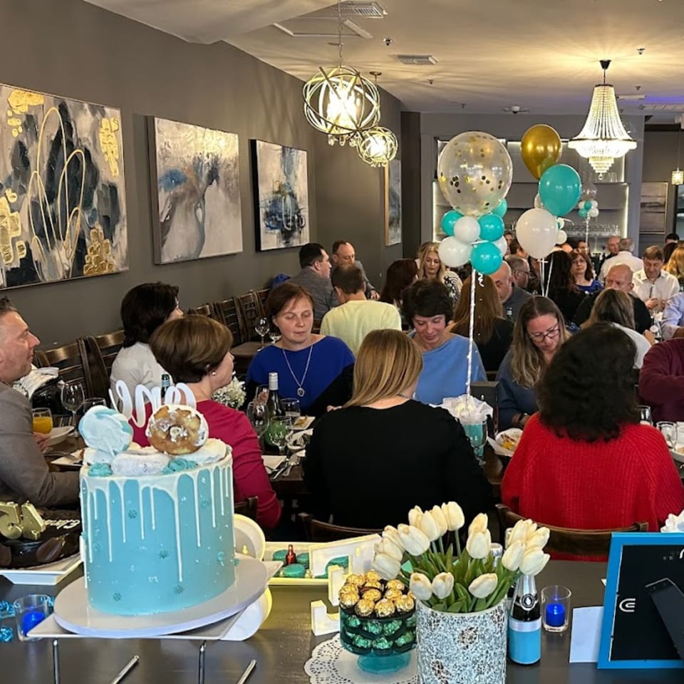 A large group of people celebrating with cakes and balloons at Parisa Persian Grill.