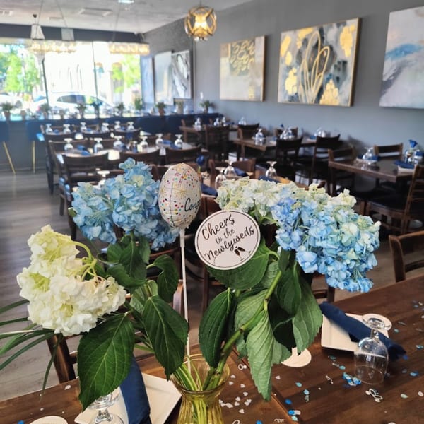 Parisa Persian Grill dining room with tables set, blue and white hydrangeas, and "Cheers to the Newlyweds" sign.